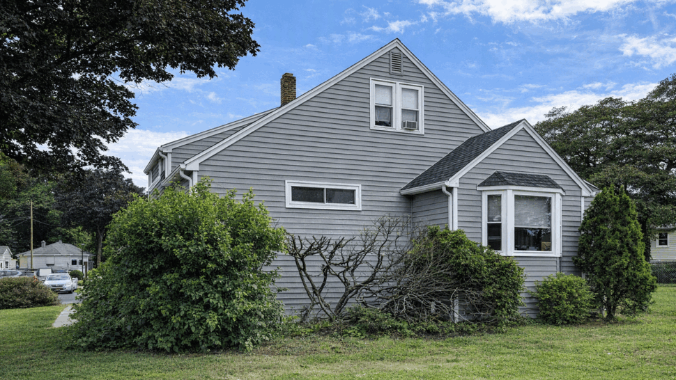 Side profile of gray vinyl siding with trimmed shrubs and small windows