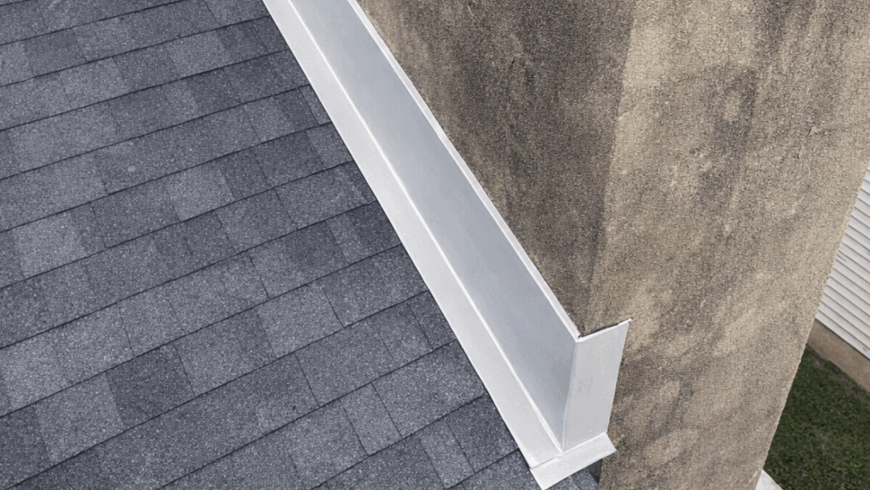 Roof Wall Flashing Detail | Tycos Roofing And Siding Inc Close-up of white metal flashing along a roof and weathered masonry wall