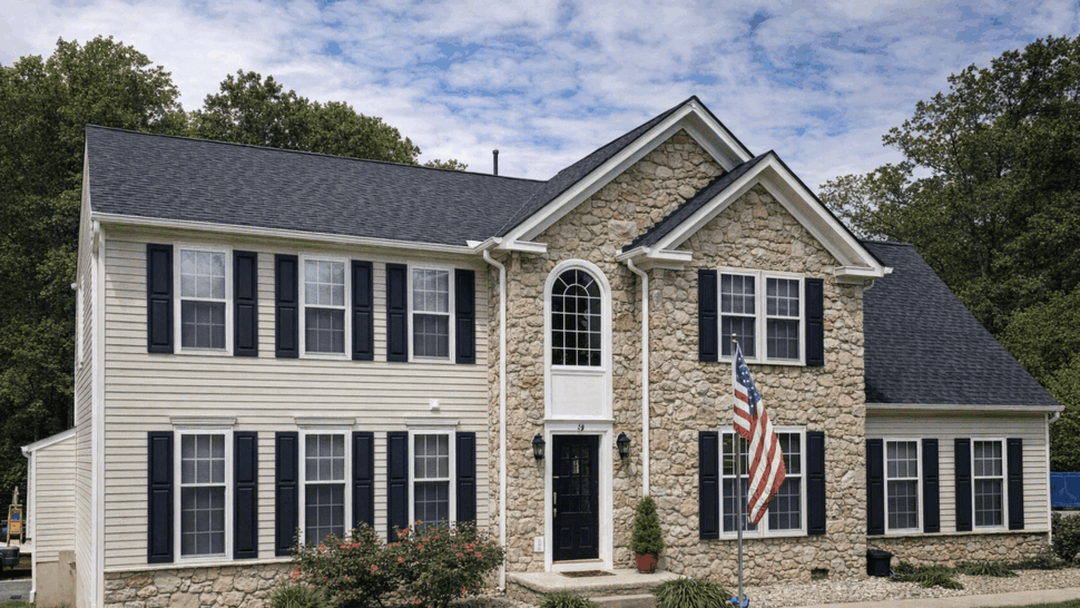 Colonial home with stone facade roof | Tycos Roofing And Siding Inc Front of colonial house with stone center, dark shingle roof and black shutters.