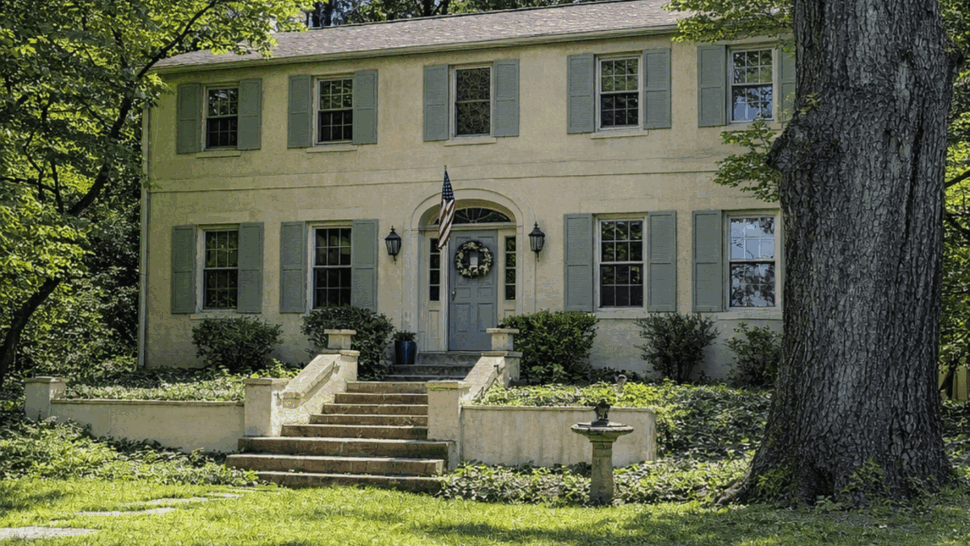 Front exterior of two-story colonial home with stucco siding and trees