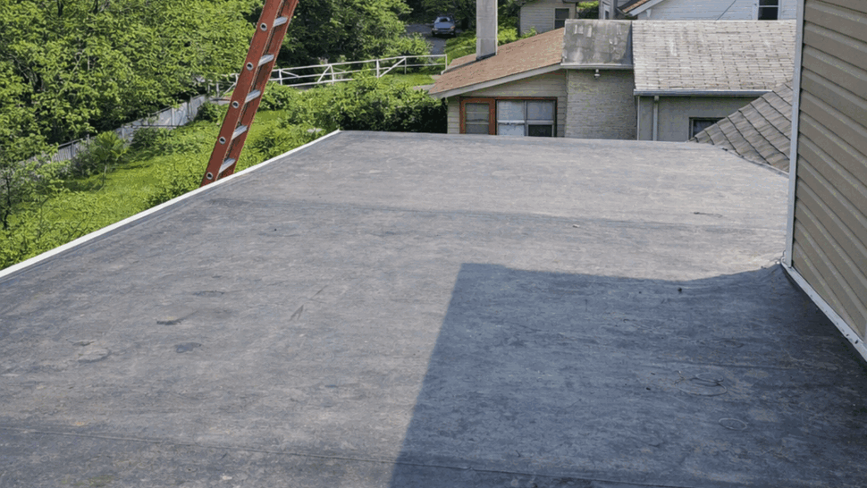 Flat gray membrane roof with a ladder and nearby houses visible