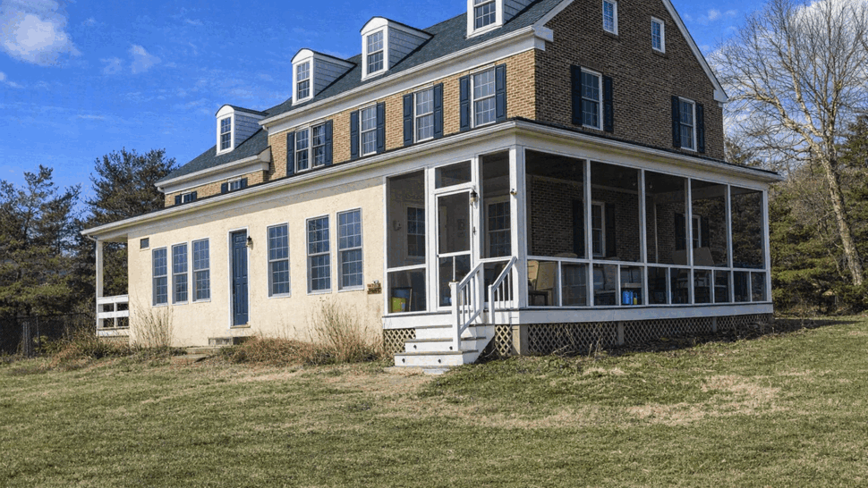 Screened four season porch on colonial home | Tycos Roofing And Siding Inc Two-story colonial house with a screened porch and green metal roof under a blue sky