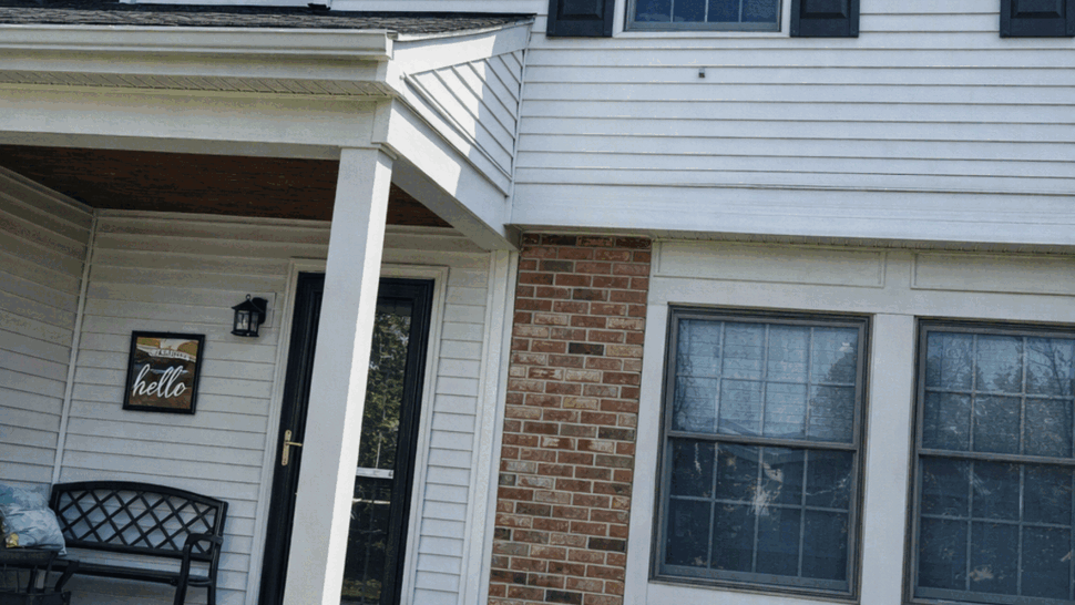 Front porch with vinyl siding, brick accent, windows and entry door.