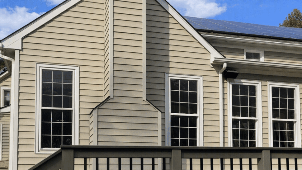 Beige sided house exterior with chimney, windows and deck railing.