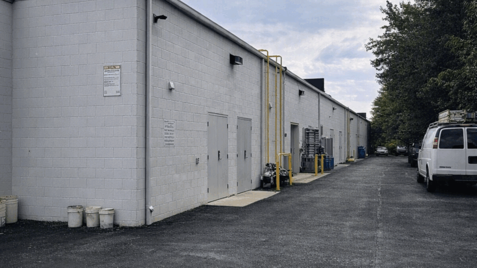 Long alley beside a white commercial building with flat roof and asphalt under cloudy sky.