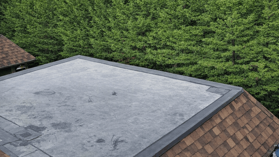 Gray flat roof section bordered by brown architectural shingles.