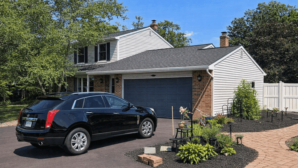 Two-story home with attached garage, black SUV in driveway and a dark shingled roof.