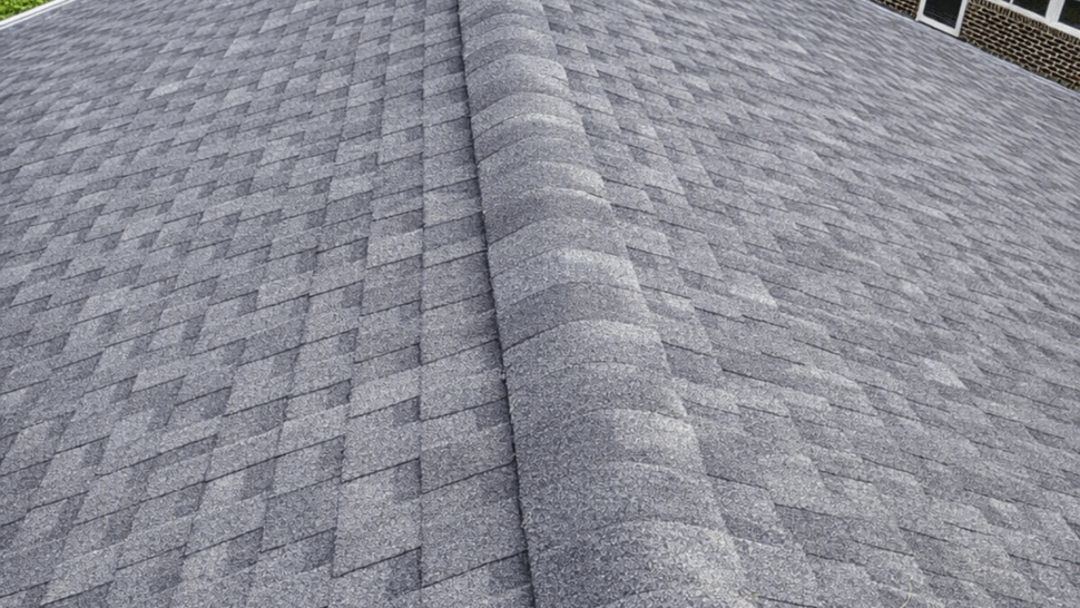 Close-up view down a gray asphalt shingle ridge on a residential roof