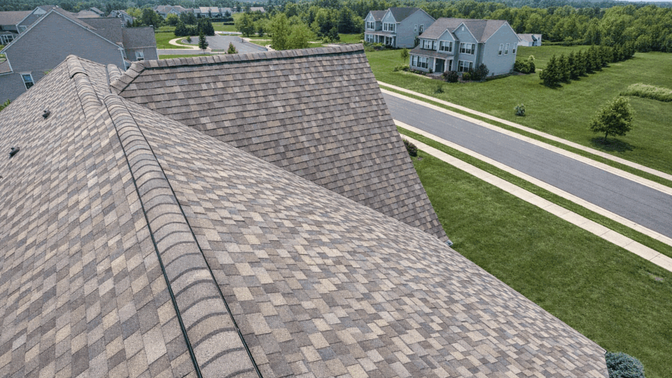Aerial close-up of asphalt shingles, ridge cap, and ventilation on a residential roof.