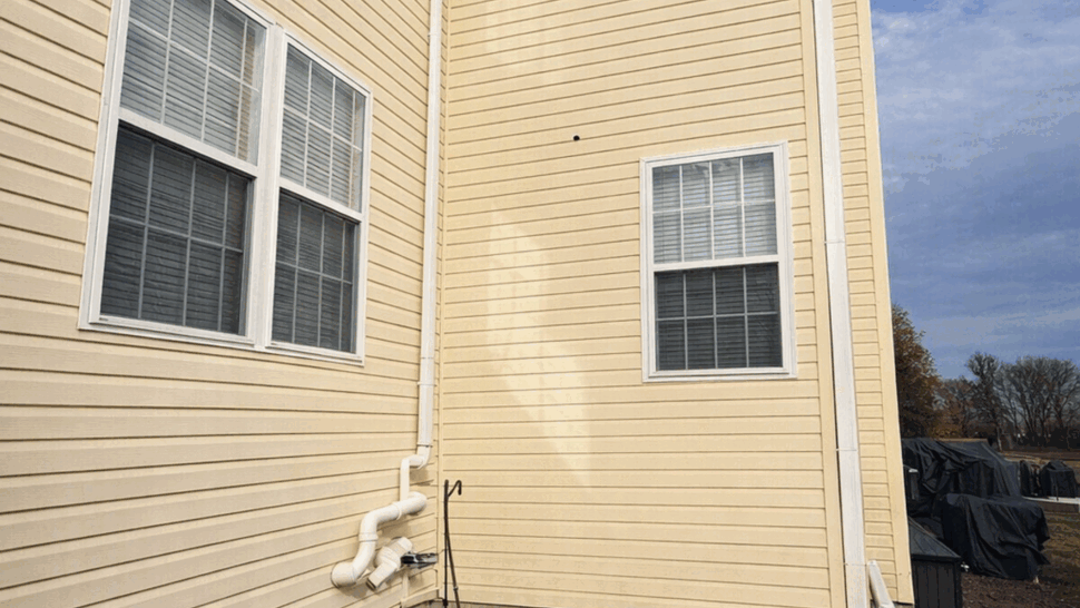 Close-up of beige vinyl siding by basement window with drainage pipes