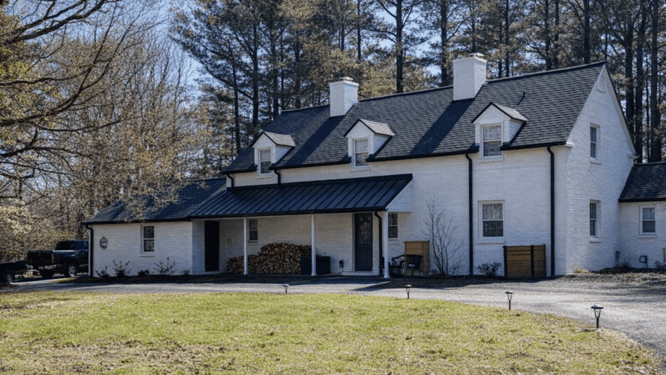 Front porch with black metal awning roof and shingled upper roof on white house.