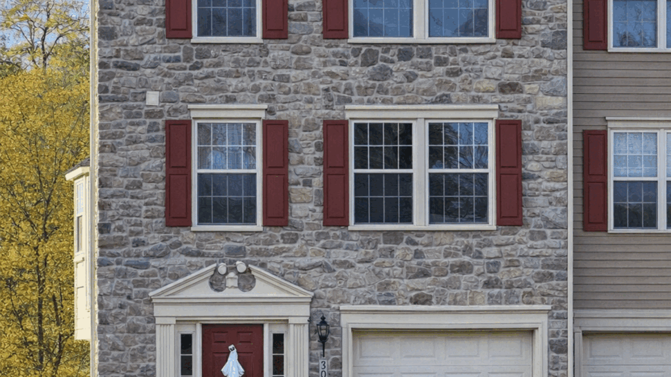 Stone Facade Townhouse Siding | Tycos Roofing And Siding Inc Three-story townhouse with stone facade, red shutters, and attached garage.