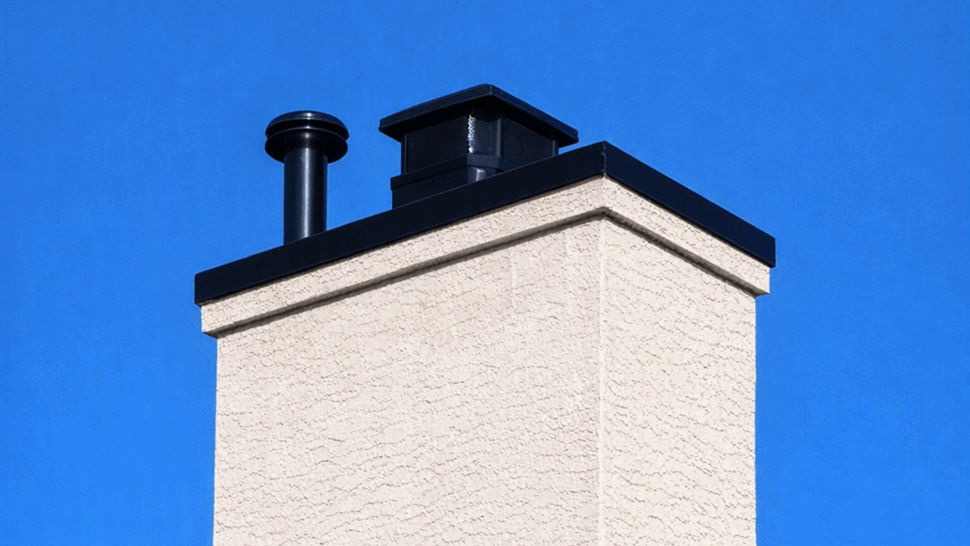 Stucco chimney with black metal flues and cap against clear sky
