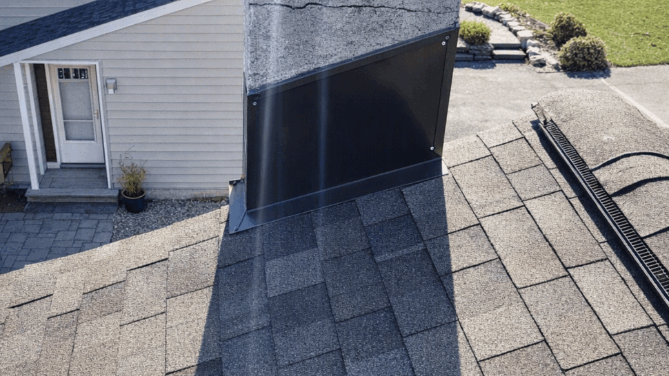 Close-up of chimney base with metal flashing and asphalt shingles on roof.