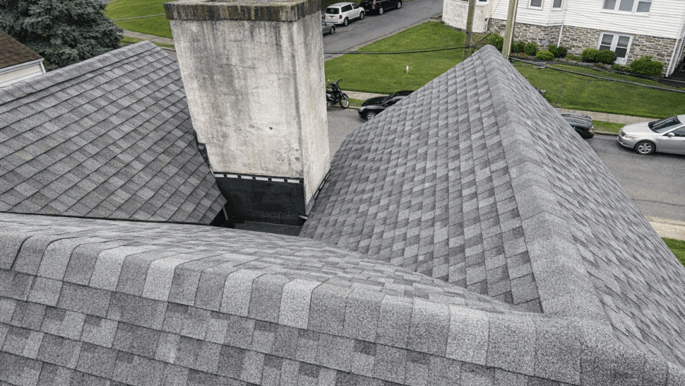 Close-up aerial view of intersecting gray shingle roofs and a chimney.