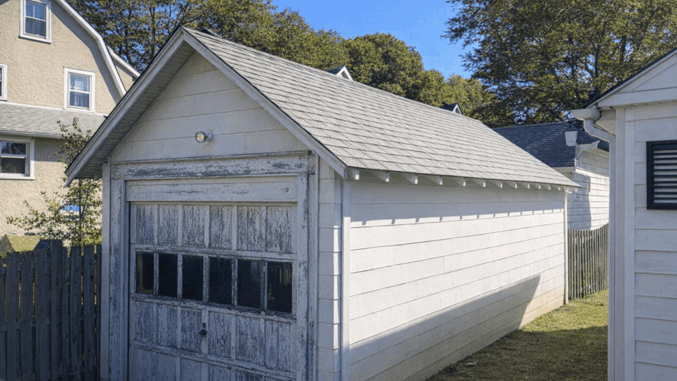 Old detached garage with peeling wooden overhead door and small shingled gable