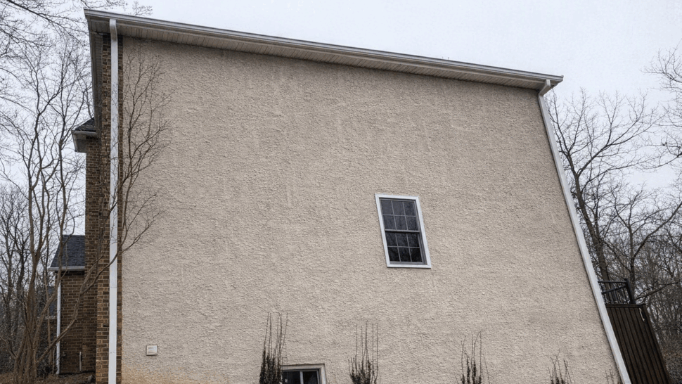 Stucco Sidewall and Gutters | Tycos Roofing And Siding Inc Tall stucco side wall with single window and white gutter running along roof