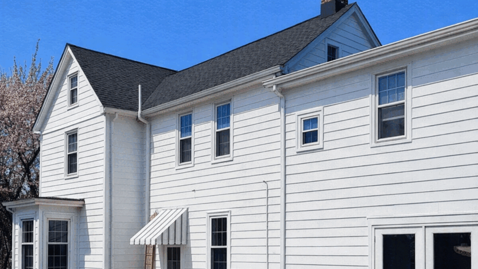 Rear Exterior with Siding and Gutters | Tycos Roofing And Siding Inc White two-story house exterior with pool cover and visible gutters.