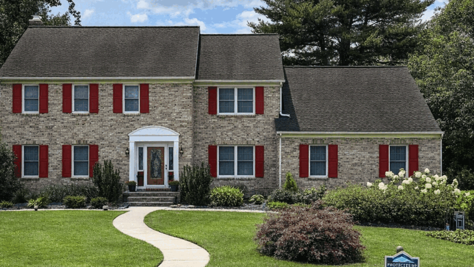 Brick colonial house with large lawn and shingled roof under blue sky