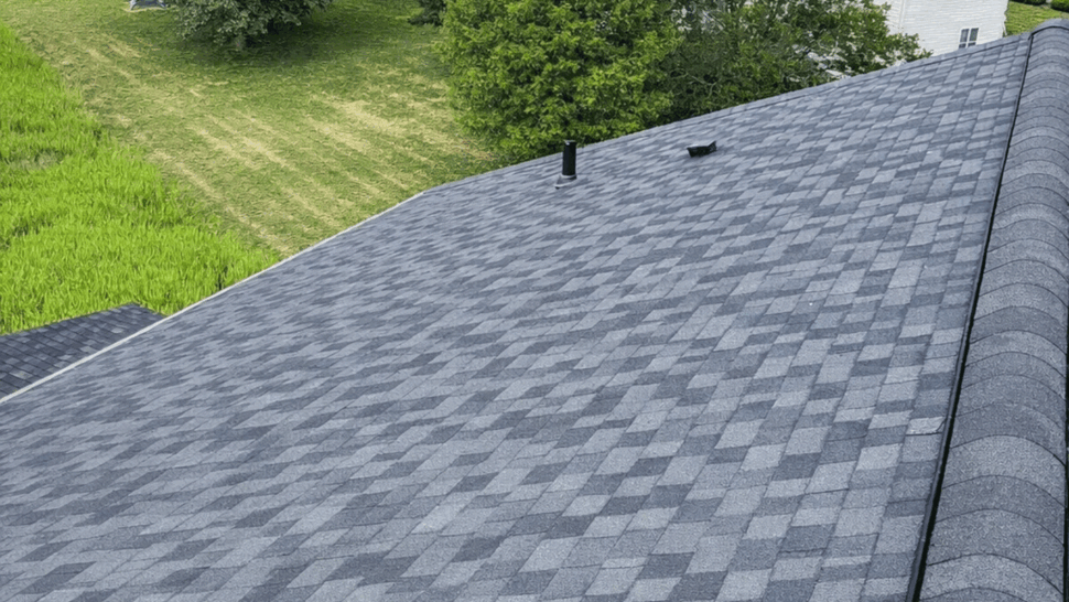 Aerial Roof Slope with Ridge Vent | Tycos Roofing And Siding Inc Aerial view of a shingled roof slope and ridge vent overlooking neighboring yards and trees.