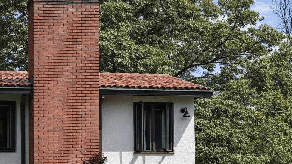 Brick chimney next to stucco siding and red tile roof edge