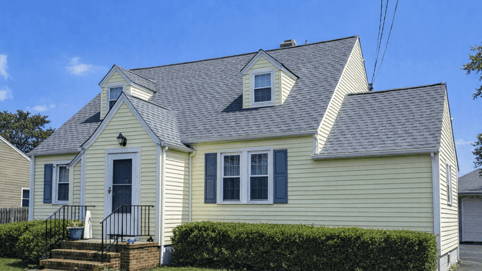Green home with gray shingle roof and light siding under a blue sky
