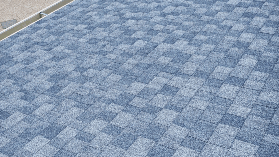 Shingle and Gutter Close-up | Tycos Roofing And Siding Inc Close-up of gray asphalt shingles and a clean metal gutter along a backyard roof edge.