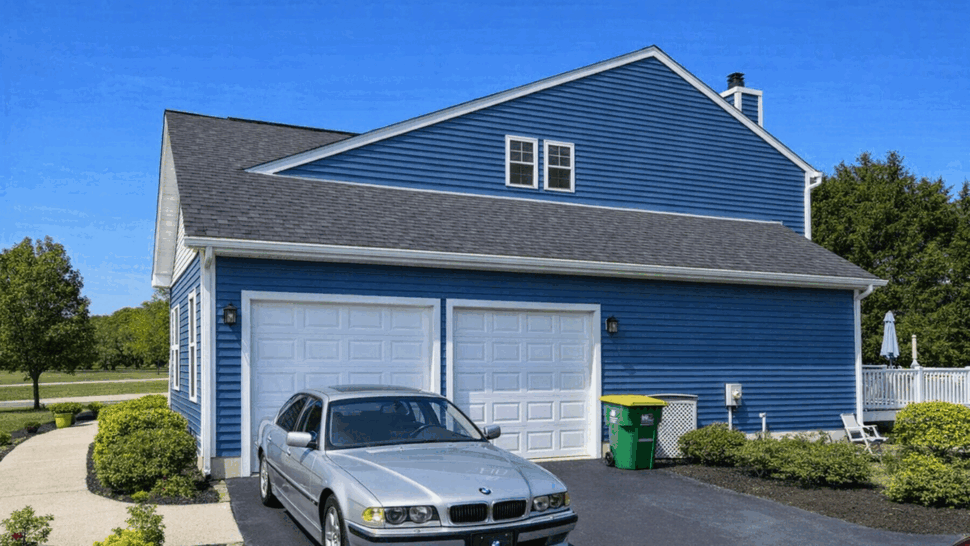 Garage Side Gutters and Siding | Tycos Roofing And Siding Inc Side view of a blue house garage with white gutters and a parked car in the driveway.