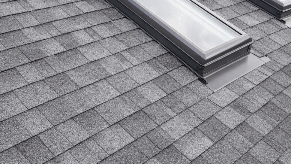 Close-up skylights with flashing | Tycos Roofing And Siding Inc Close-up of two skylights with metal flashing set into gray asphalt shingles.