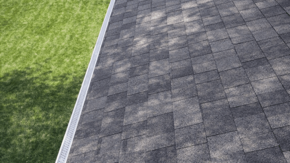 Top-down view of dark gray asphalt shingle roof and gutter edge above a green yard.