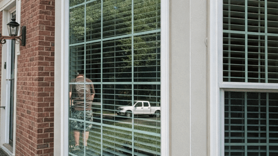 Close-up of bay window glass and white trim with reflected vehicle.