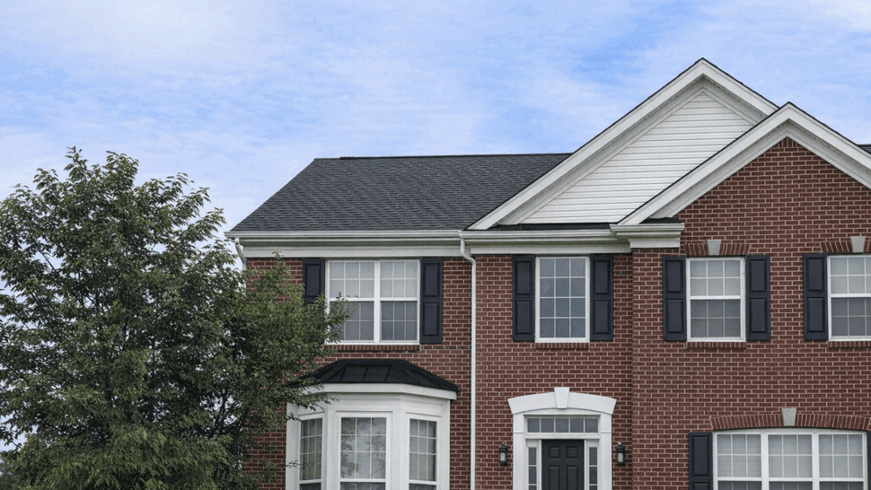 Two-story brick house with dark shingle roof, white gutters and black shutters.
