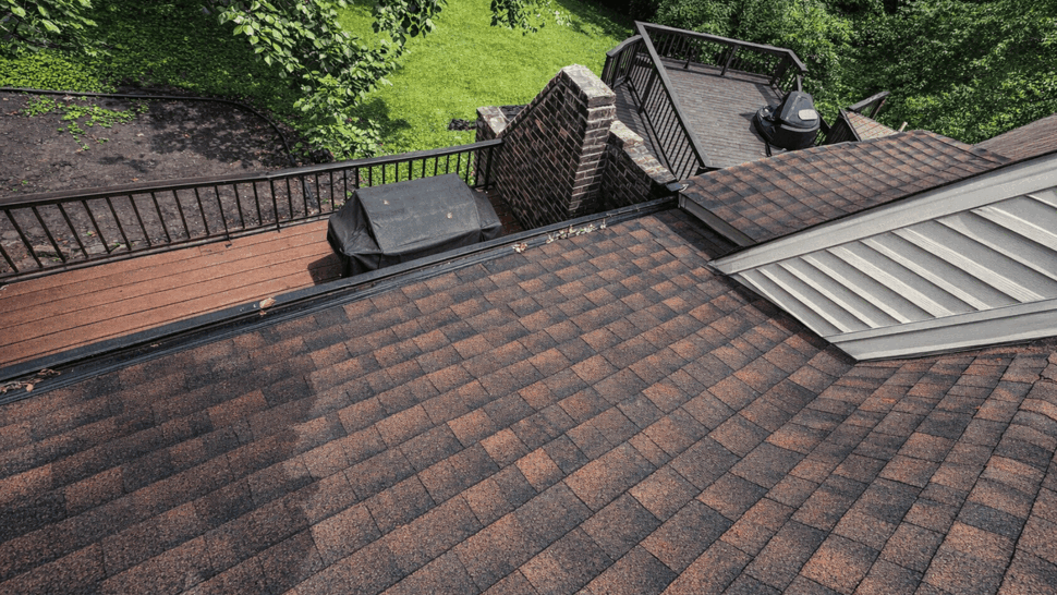 Top-down view of asphalt shingle roof with deck and railings below.