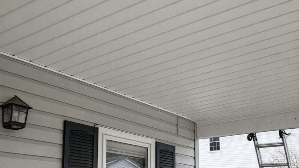 Covered Porch Soffit and Siding | Tycos Roofing And Siding Inc Covered porch with white soffit, gray siding, window, shutters, and ladder.