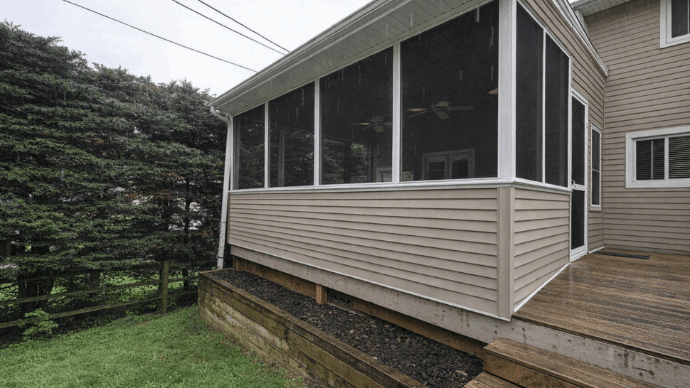 Elevated screened porch with beige siding and lawn below.