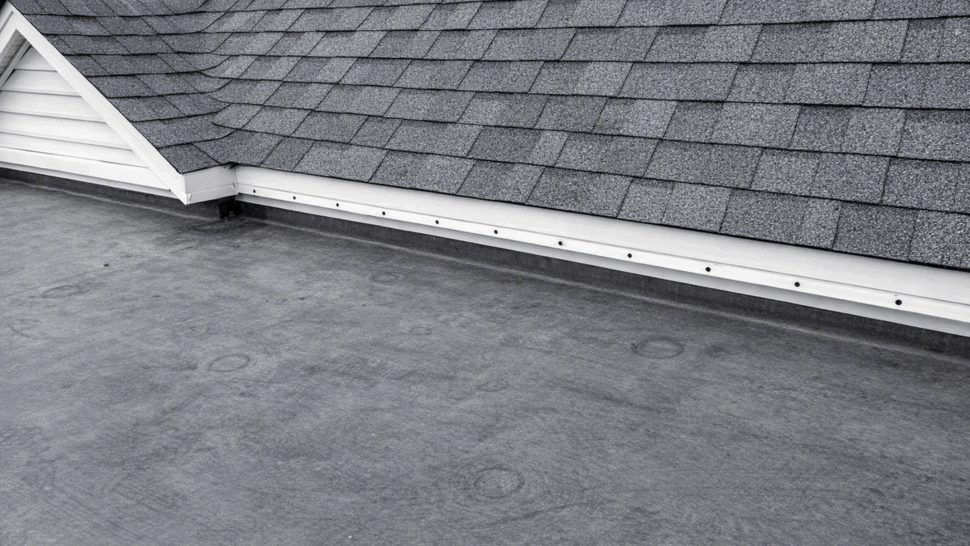 Detail of metal roof flashing where a shingle roof meets a flat rubber membrane roof surface.