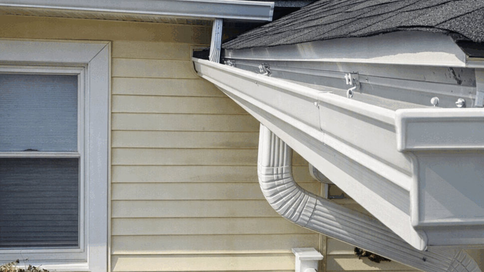 Gutter Corner and Downspout Detail | Tycos Roofing And Siding Inc White gutter and curved downspout at roof corner above porch steps.