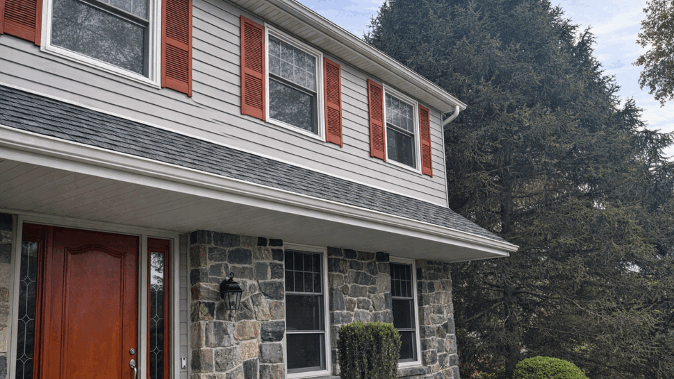 Red front door with stone lower facade, vinyl siding and red shutters.