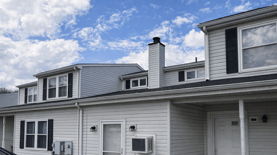Residential Siding and Gutter Detail | Tycos Roofing And Siding Inc Gray home siding with gutters, windows, exterior door, and air conditioner.