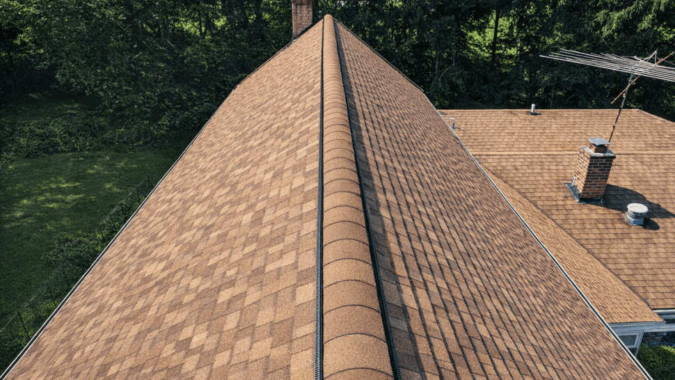 Aerial roof ridge and chimney view | Tycos Roofing And Siding Inc Aerial view along roof ridge showing uniform brown shingles and two chimneys.