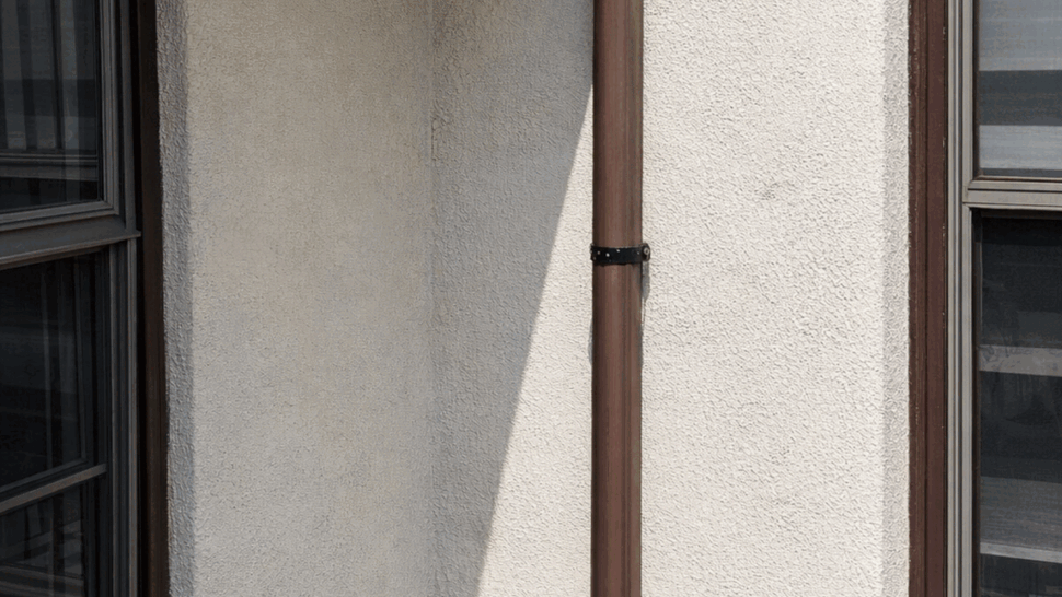 Downspout base at roof corner with flashing and shingle edge visible