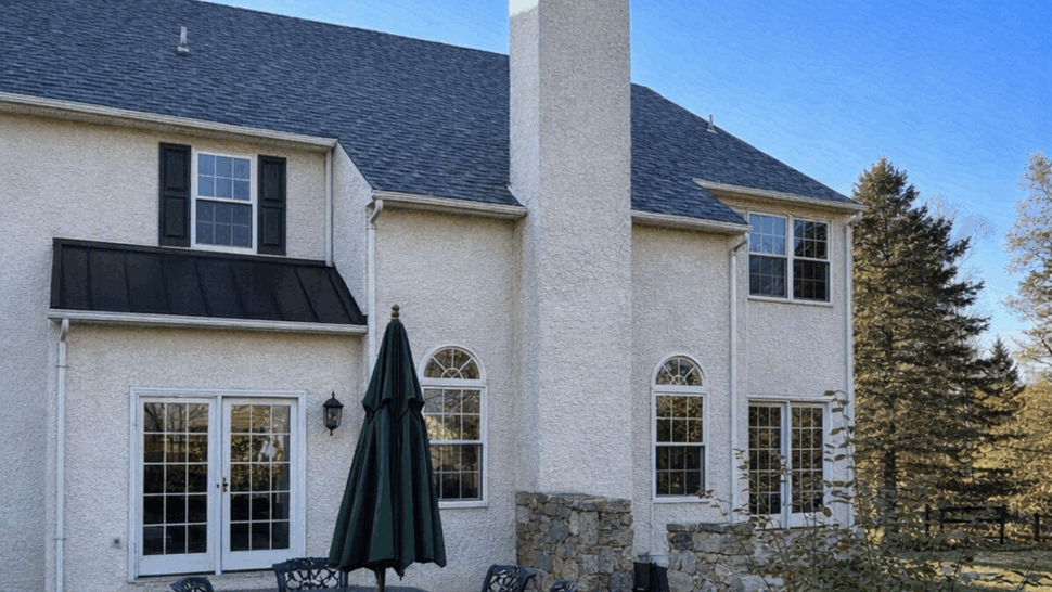 Two-story home with dormer roof, stucco siding and landscaping under clear blue sky