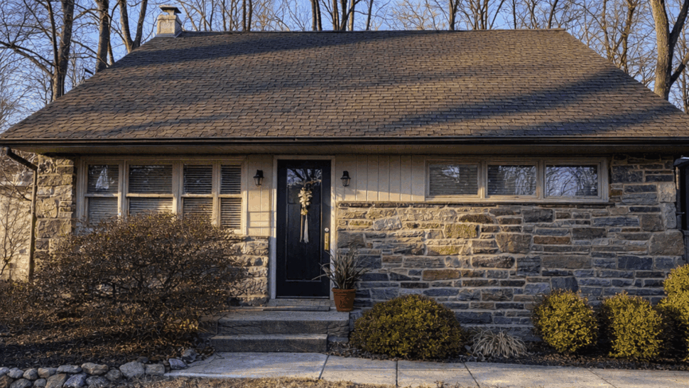 Front view of single-story stone house with shingled roof and entry