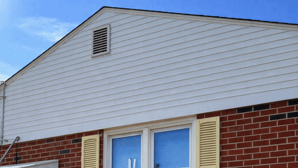 White gable vinyl siding above brick wall with double window and shutters