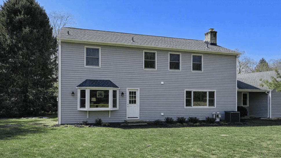 Rear view of two-story house with gray asphalt roof and vinyl siding.
