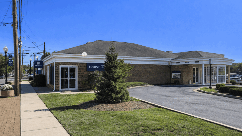Brick bank building with pitched roof and drive-through canopy on a sunny day