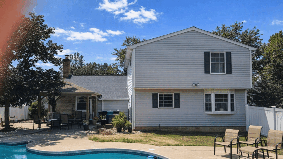 Backyard pool beside a two-story house showing light siding and patio area.