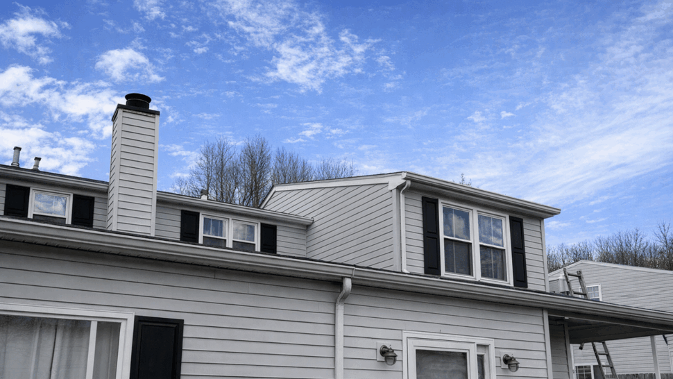 Gray Siding Home Exterior | Tycos Roofing And Siding Inc Gray-sided home with black shutters, windows, chimney, and gutters.