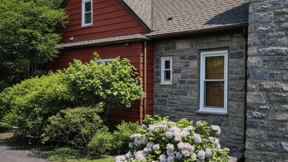 Red sided and stone exterior home with hydrangeas and driveway.