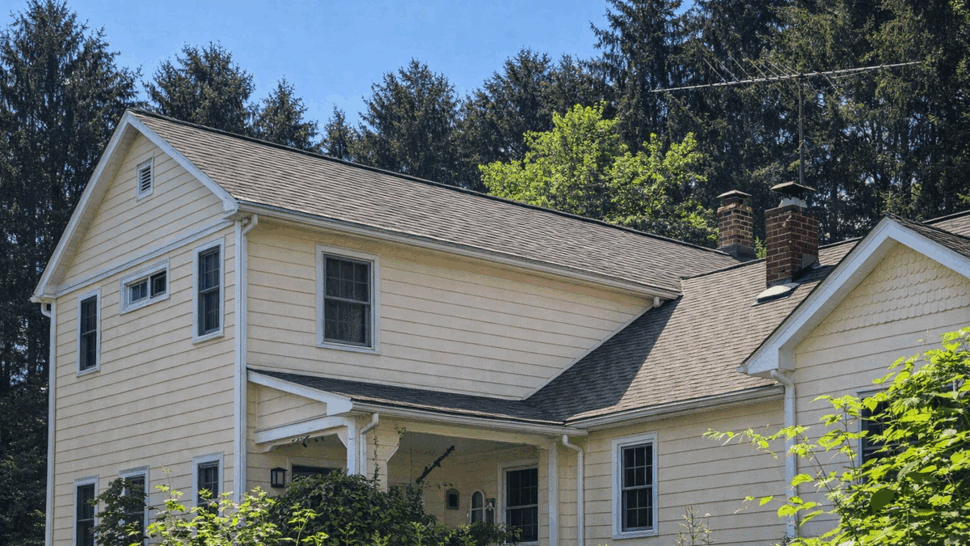 Two-story siding and gutters on home | Tycos Roofing And Siding Inc Two-story cream house with porch, white siding, gutters and dark asphalt roof.